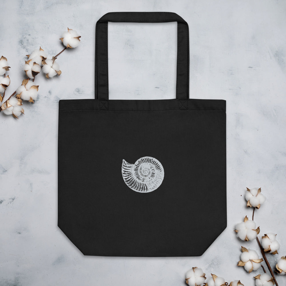 A canvas tote bag printed with a black line art illustration of a Scaphites nodosus ammonite shell. Flat lay, Ink colourway.