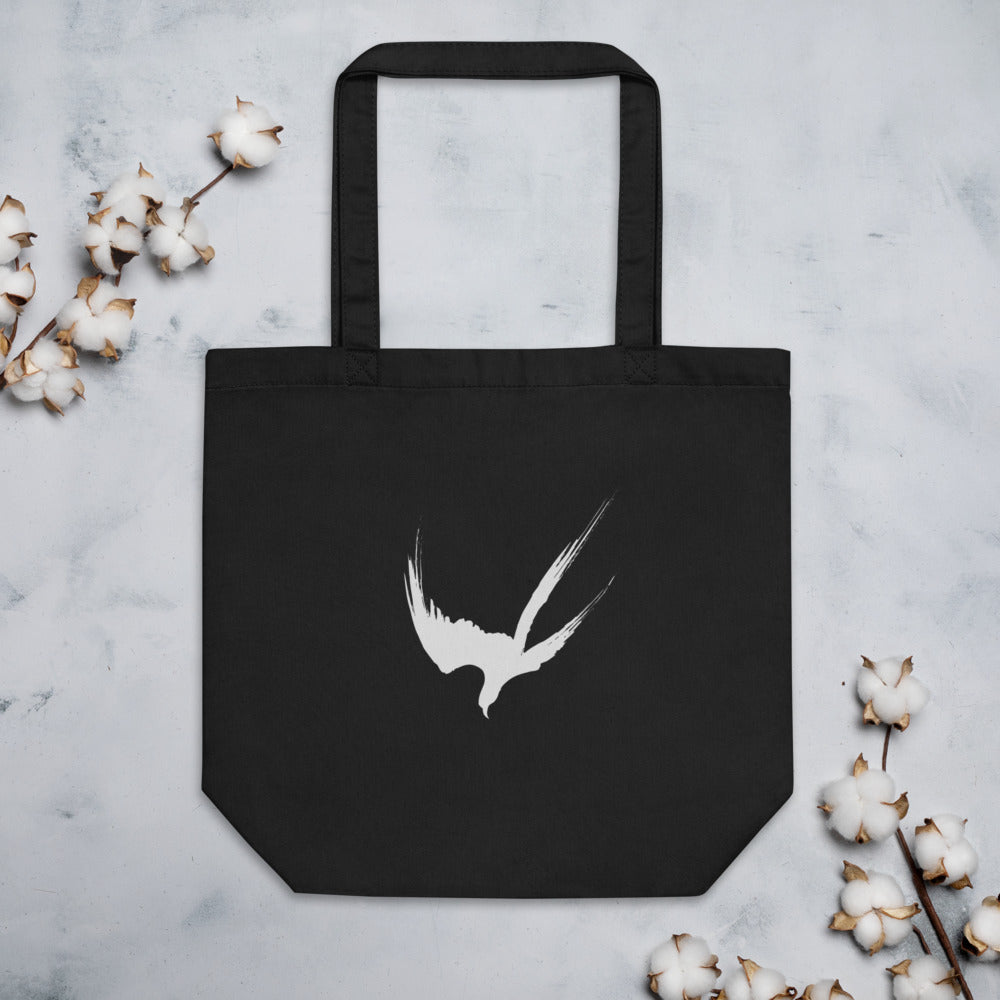 A minimalist three-stroke sumi-e hawk design with dry-brush texture printed on a tote bag. Flat lay, Ink colourway.