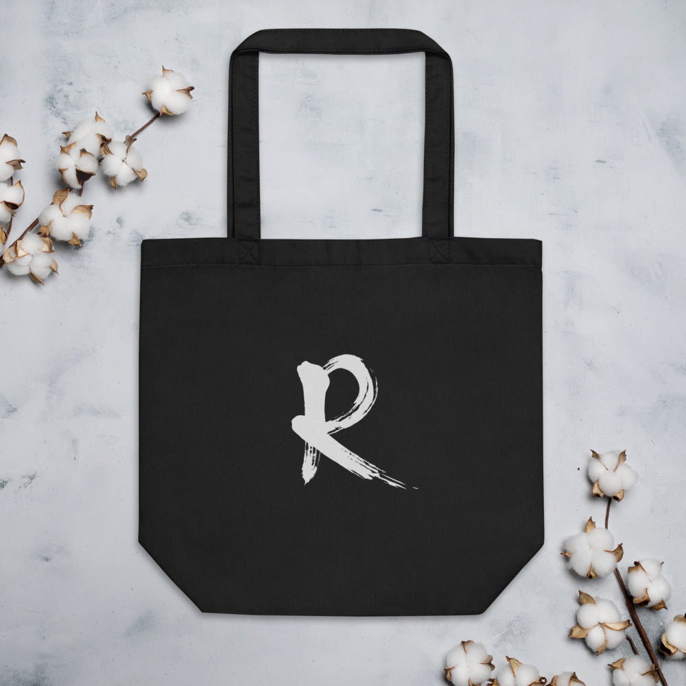 A minimalist sumi-e brush stroke design of the capital letter R printed on a tote bag. Flat lay, Ink colourway.