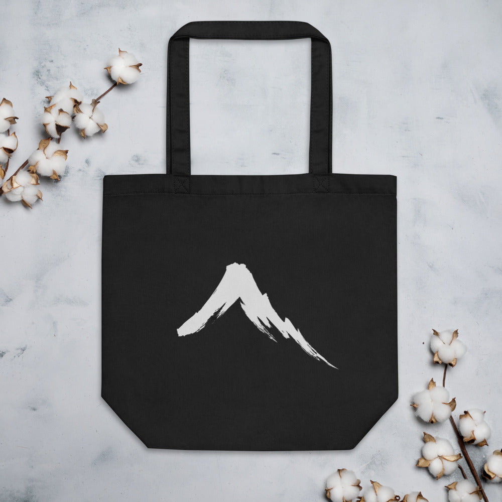 A single downward sumi-e ink brush stroke depicting a steep volcanic mountain slope on a tote bag. Flat lay, Ink colourway.