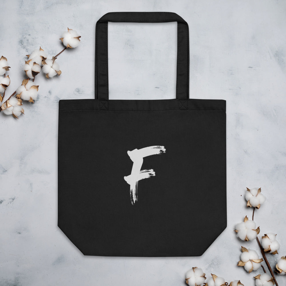 The capital letter F in bold black sumi-e brush strokes with dry-brush texture, printed on a tote bag. Flat lay, Ink colourway.