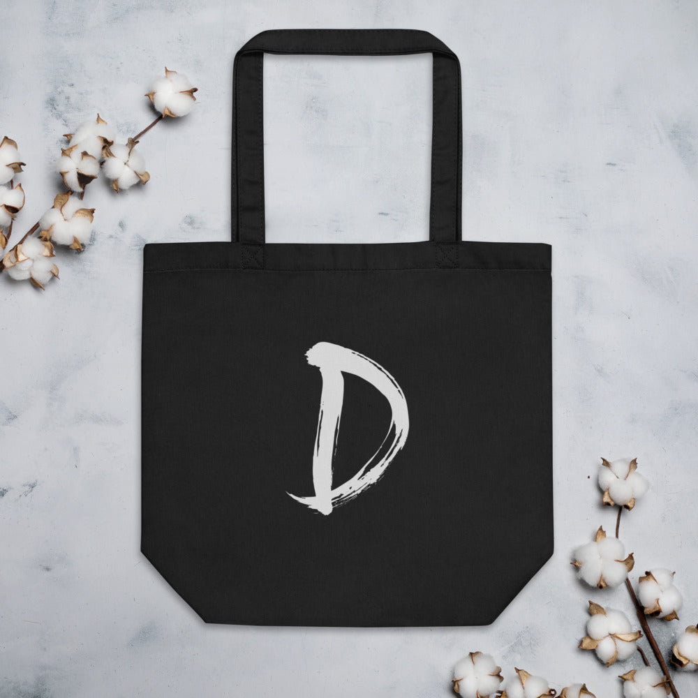 A minimalist sumi-e ink painting of the capital letter D printed on a tote bag. Flat lay, Ink colourway.