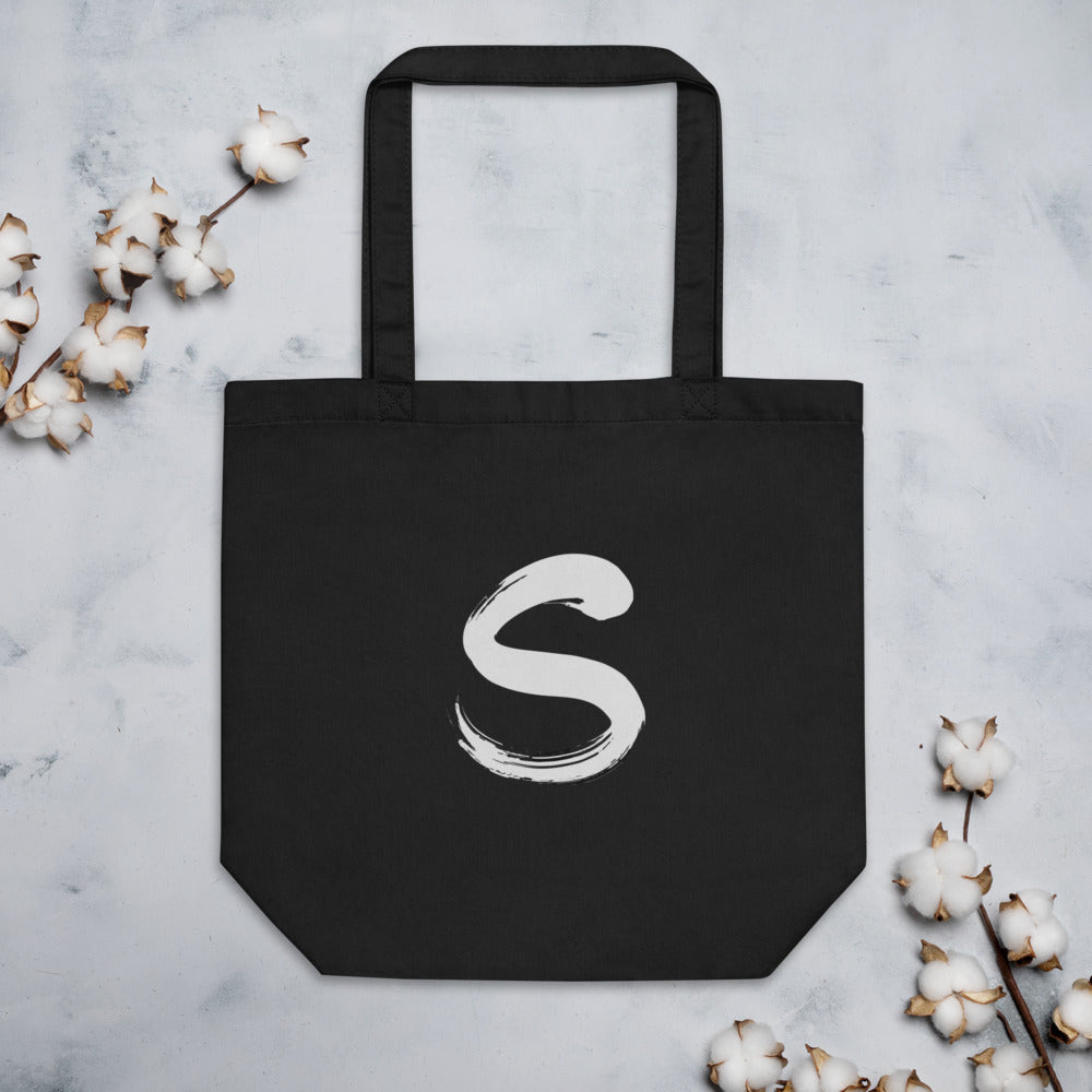 The letter S rendered in a single serpentine sumi-e brush stroke printed on a tote bag. Flat lay, Ink colourway.