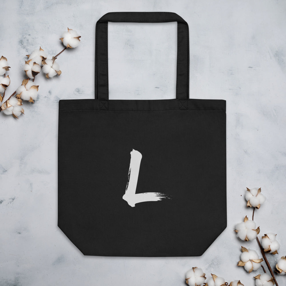 A black sumi-e brushstroke of the letter L printed on a simple tote bag. Flat lay, Ink colourway.