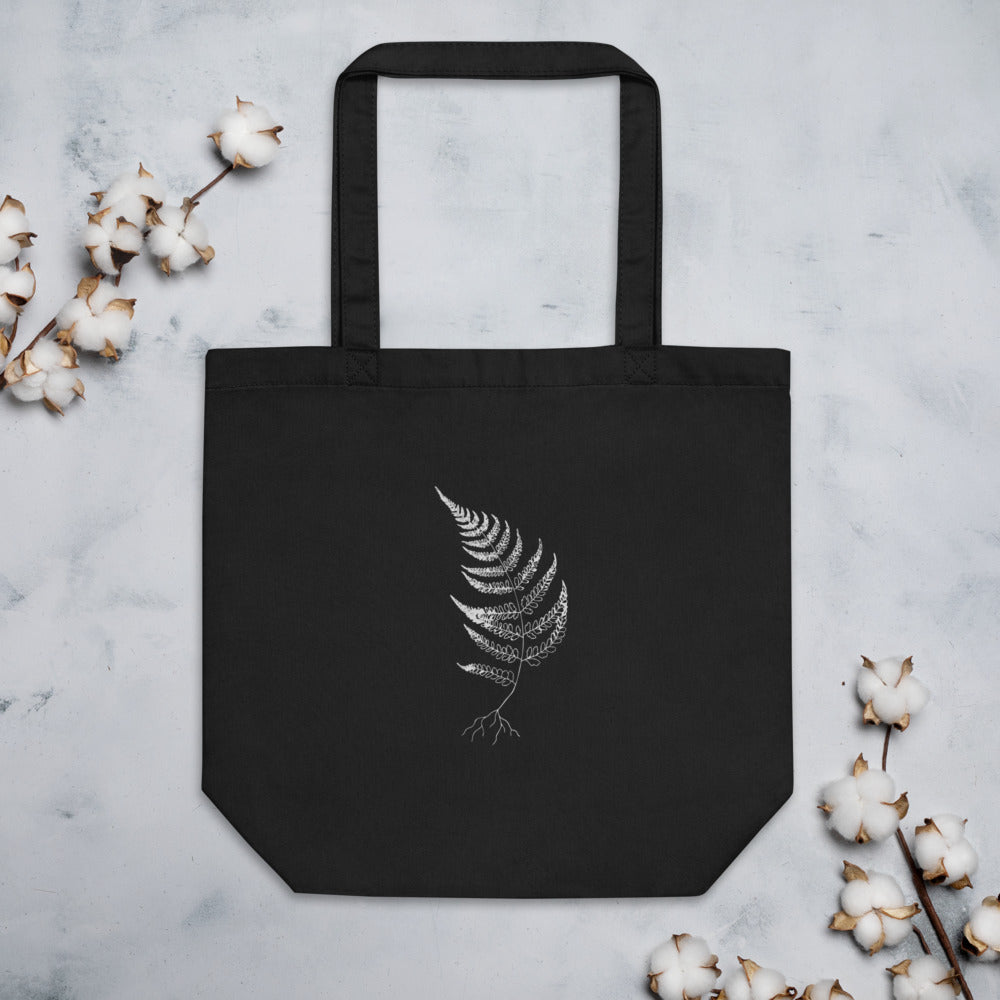 A wood fern engraving featuring detailed root structures and arched fronds, printed on a tote bag. Flat lay, Ink colourway.