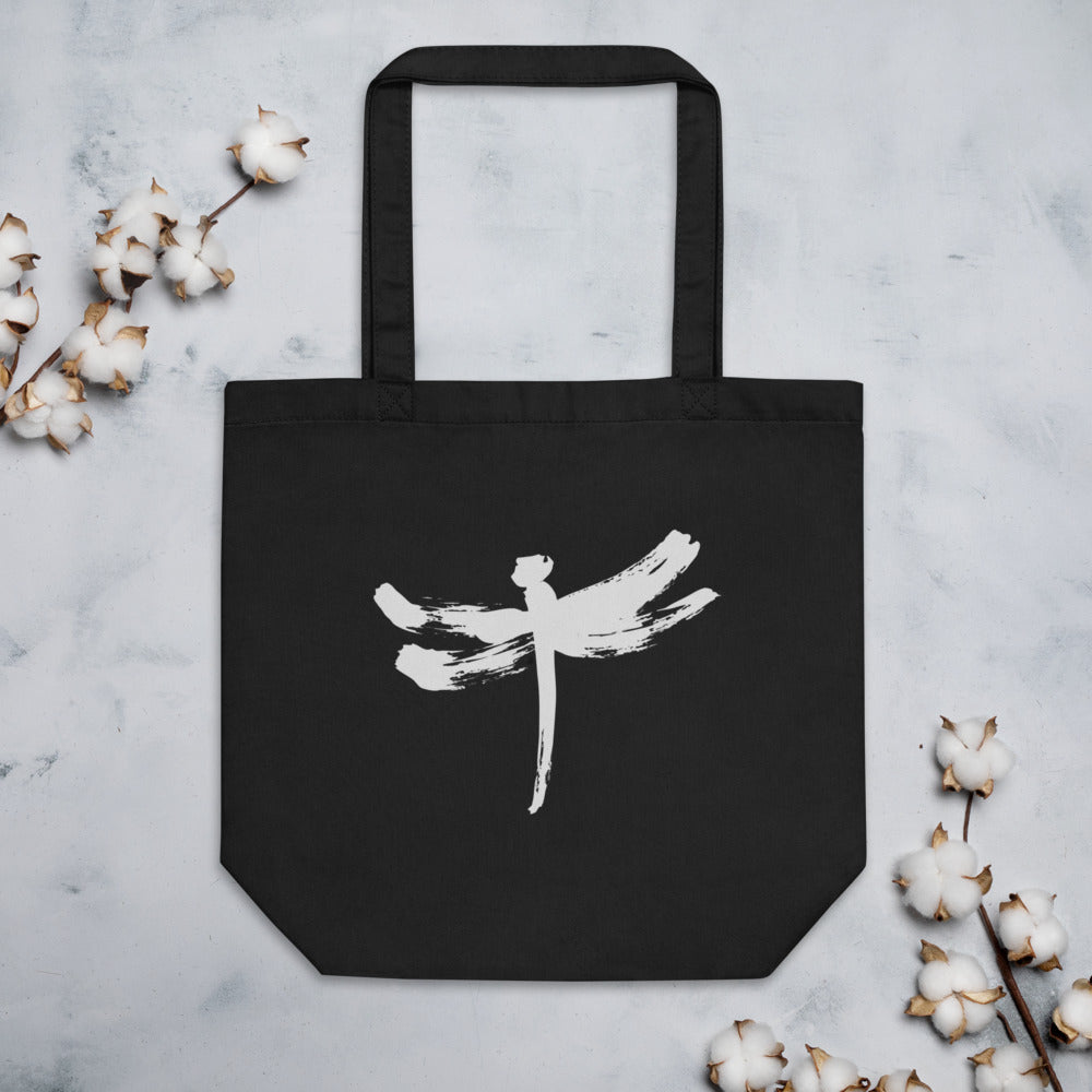 A minimalist dragonfly sumi-e ink design printed on a canvas tote bag. Flat lay, Ink colourway.