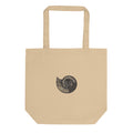 A canvas tote bag printed with a black line art illustration of a Scaphites nodosus ammonite shell. Shown on the Bone (Oyster) colorway.