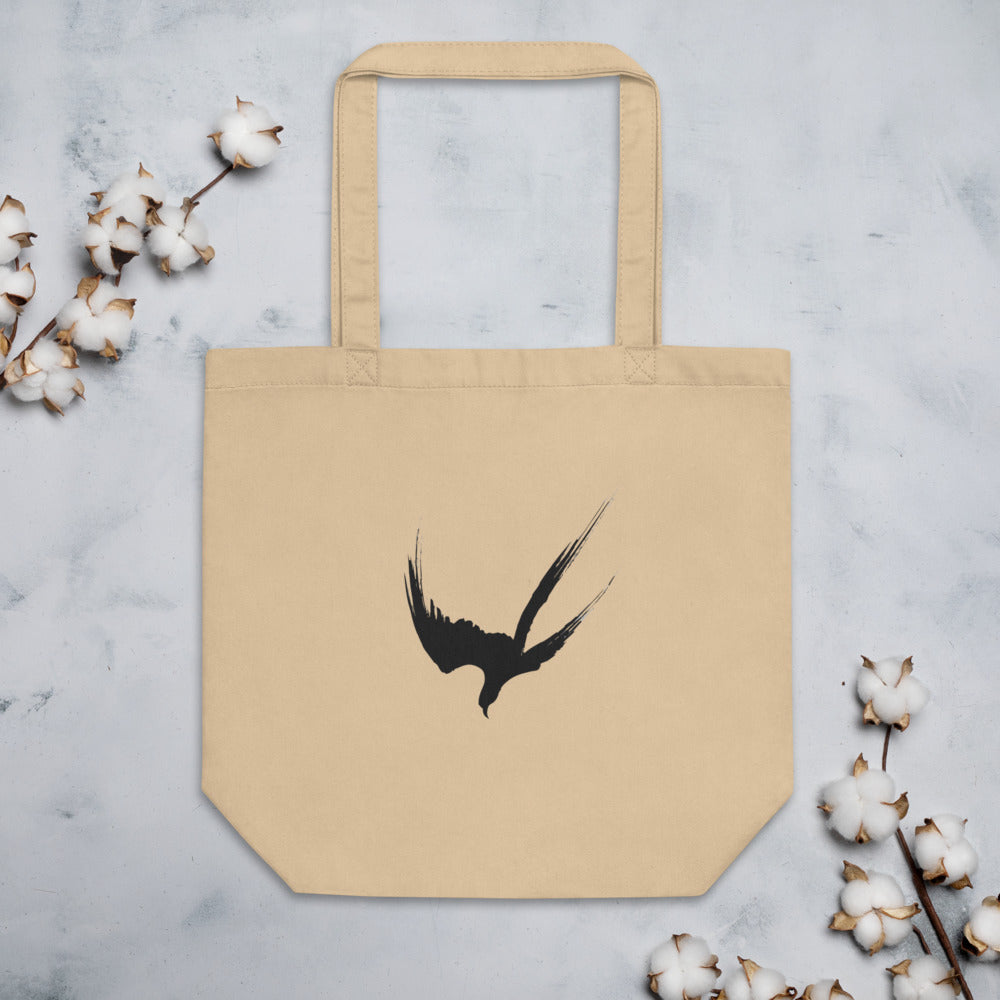 A minimalist three-stroke sumi-e hawk design with dry-brush texture printed on a tote bag. Flat lay, Bone colourway.