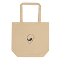 A minimalist black line art portrait of an alien visitor with a solid black almond eye on a tote bag. Shown on the Bone (Oyster) colorway.