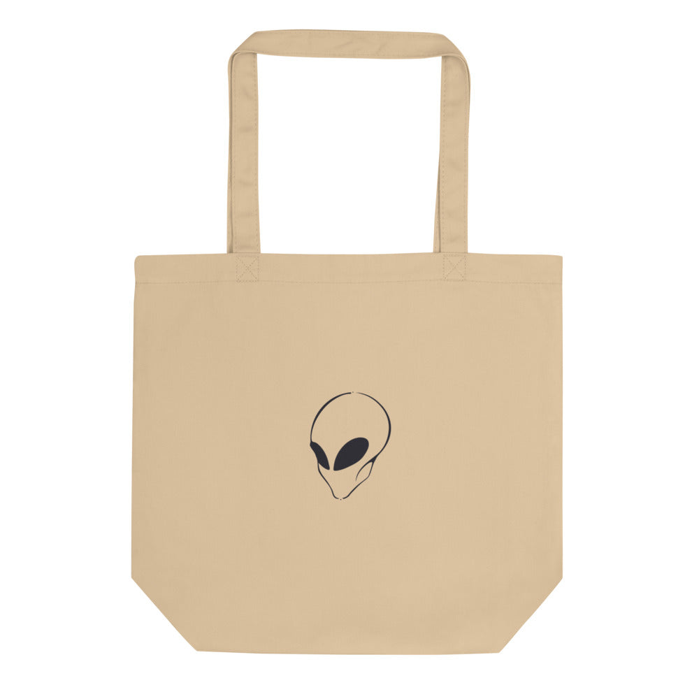 A minimalist black line art portrait of an alien visitor with a solid black almond eye on a tote bag. Shown on the Bone (Oyster) colorway.