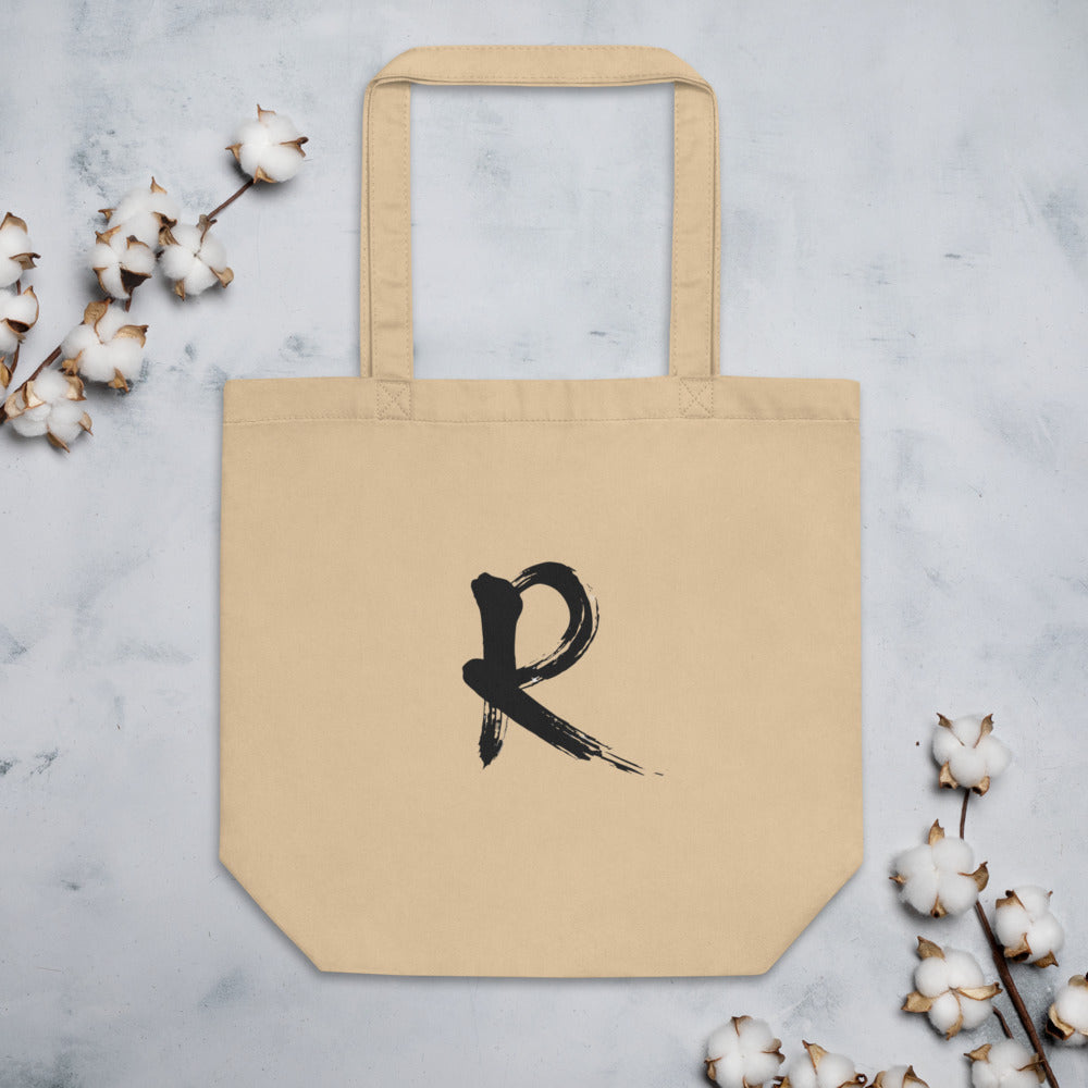 A minimalist sumi-e brush stroke design of the capital letter R printed on a tote bag. Flat lay, Bone colourway.
