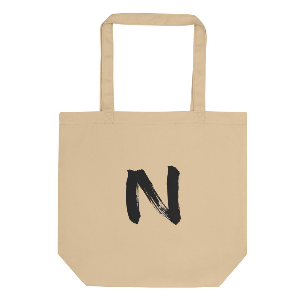 A minimal black sumi-e ink brush stroke of the letter N printed on a canvas tote bag. Shown on the Bone (Oyster) colorway.