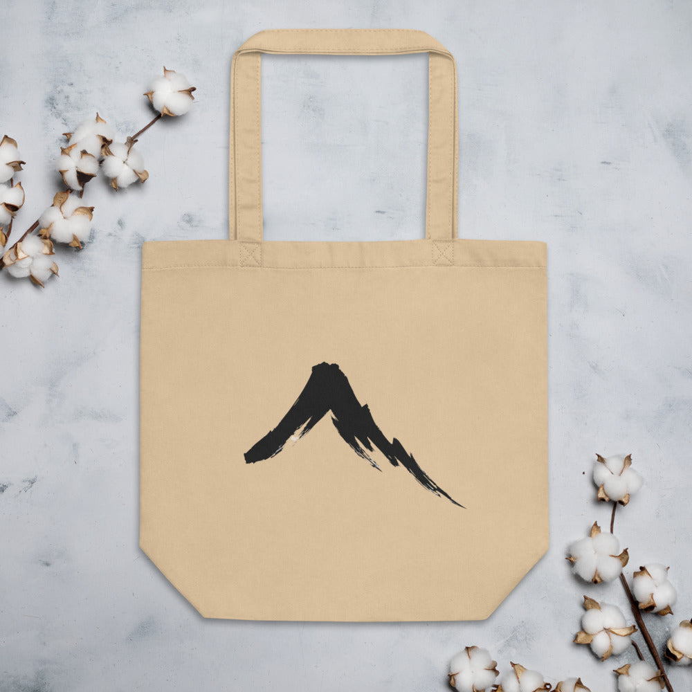 A single downward sumi-e ink brush stroke depicting a steep volcanic mountain slope on a tote bag. Flat lay, Bone colourway.