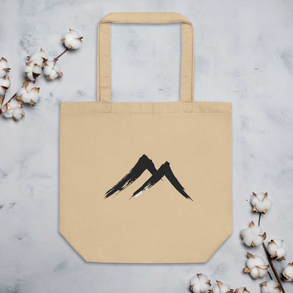 A sharp, two-stroke sumi-e mountain peak design printed on a tote bag. Flat lay, Bone colourway.