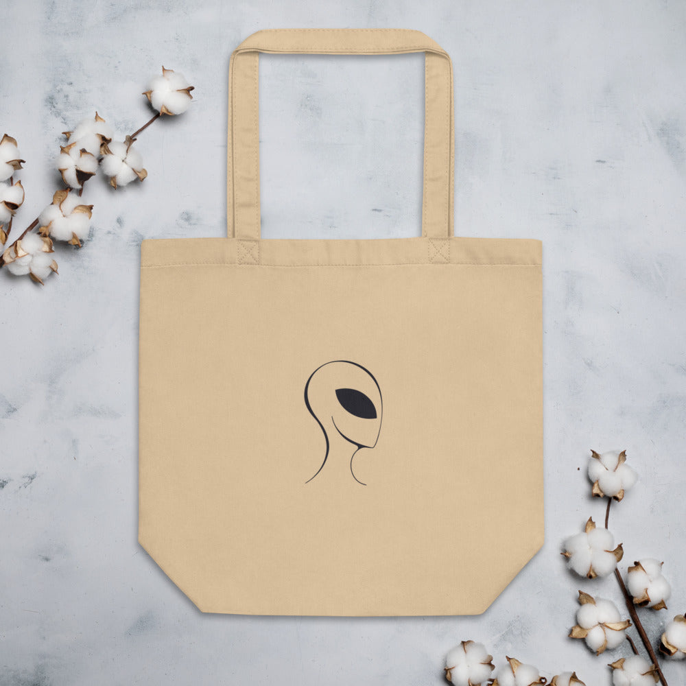 A clean line drawing of an alien visitor profile with a solid black almond-shaped eye printed on a tote bag. Flat lay, Bone colourway.