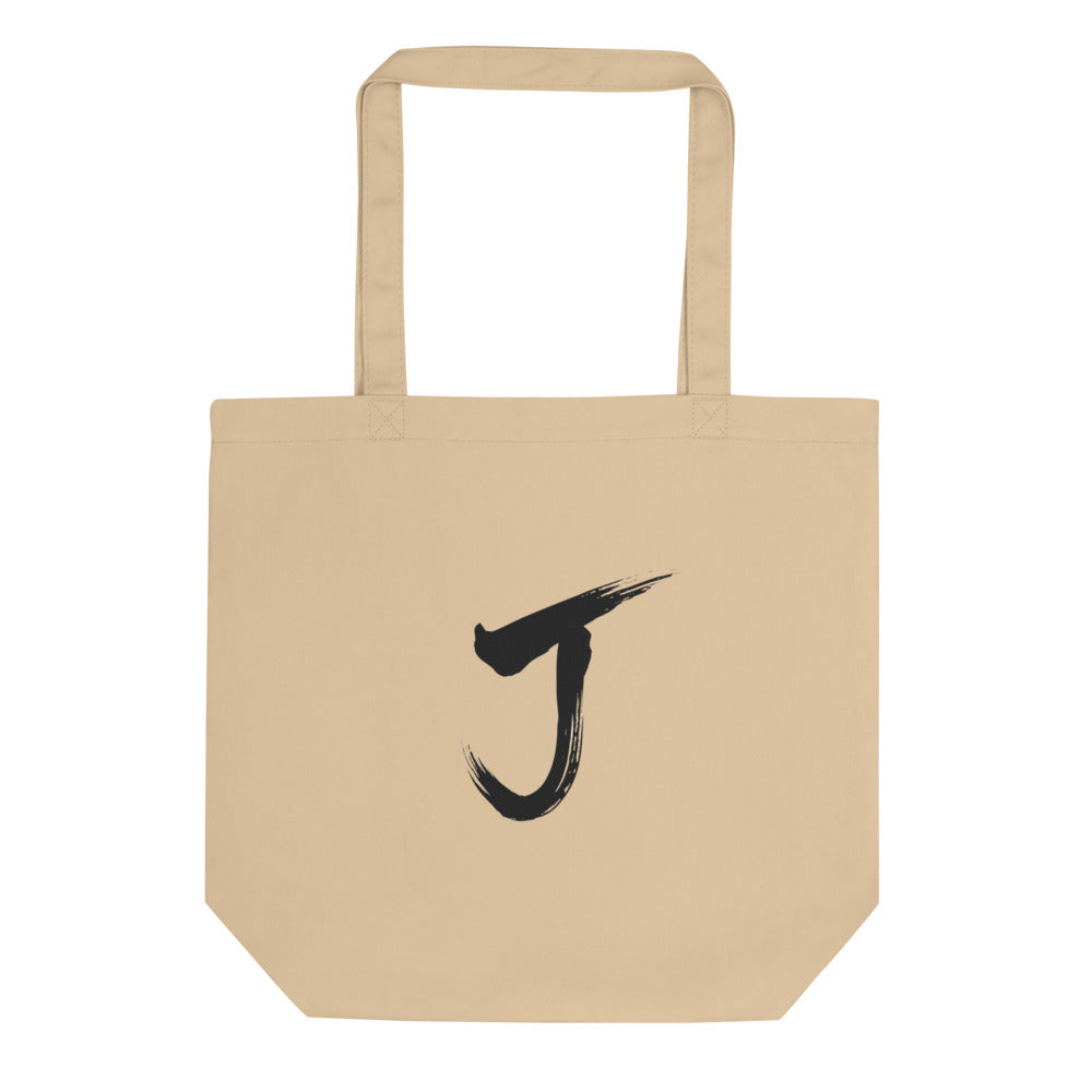 The letter J rendered in a single black sumi-e brush gesture, printed on a canvas tote bag. Shown on the Bone (Oyster) colorway.