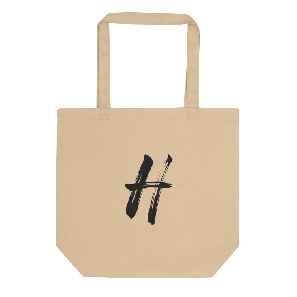 The capital letter H rendered in black sumi-e brushstrokes printed on a tote bag. Shown on the Bone (Oyster) colorway.