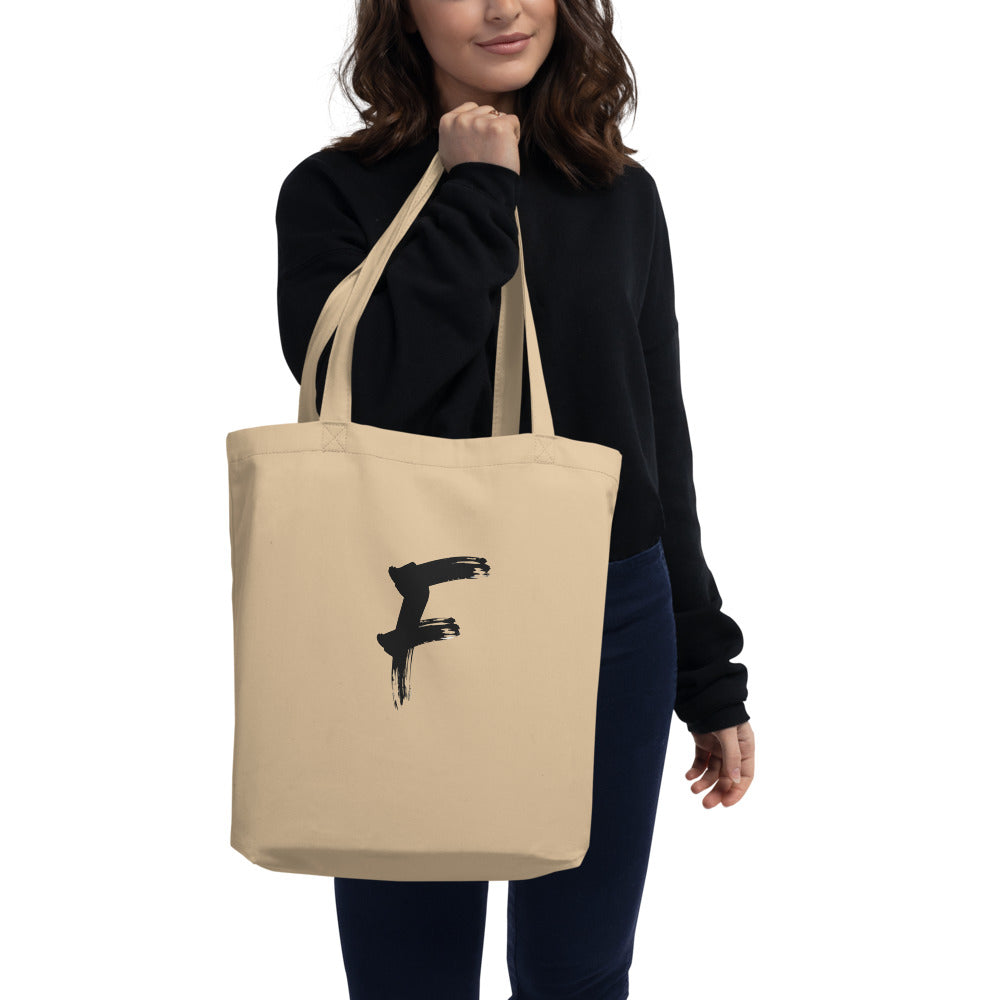 The capital letter F in bold black sumi-e brush strokes with dry-brush texture, printed on a tote bag. Carried over the shoulder, Bone colourway.
