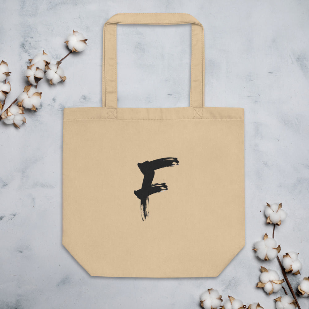 The capital letter F in bold black sumi-e brush strokes with dry-brush texture, printed on a tote bag. Flat lay, Bone colourway.