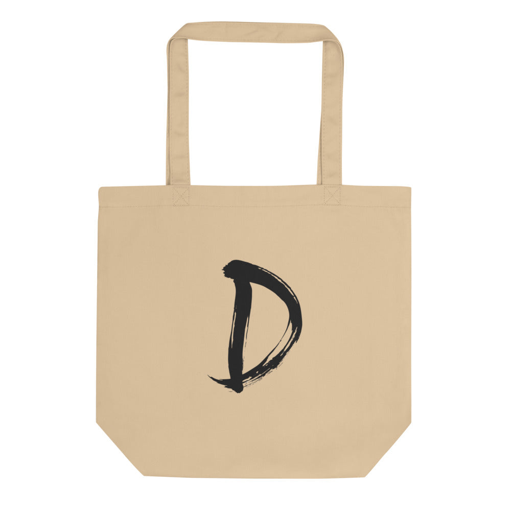 A minimalist sumi-e ink painting of the capital letter D printed on a tote bag. Shown on the Bone (Oyster) colorway.