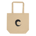 The capital letter C printed as a black sumi-e brush gesture on a tote bag. Shown on the Bone (Oyster) colorway.