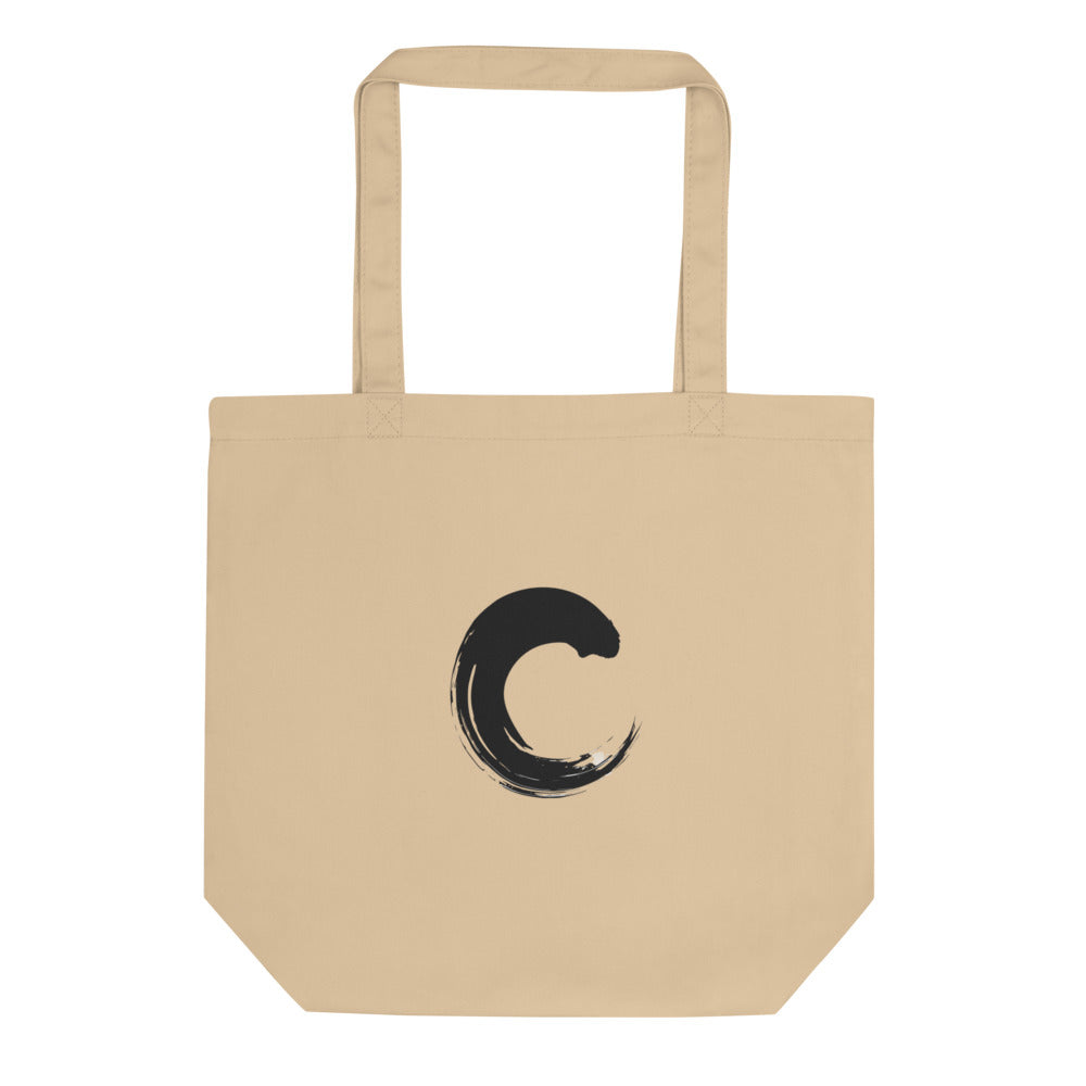The capital letter C printed as a black sumi-e brush gesture on a tote bag. Shown on the Bone (Oyster) colorway.