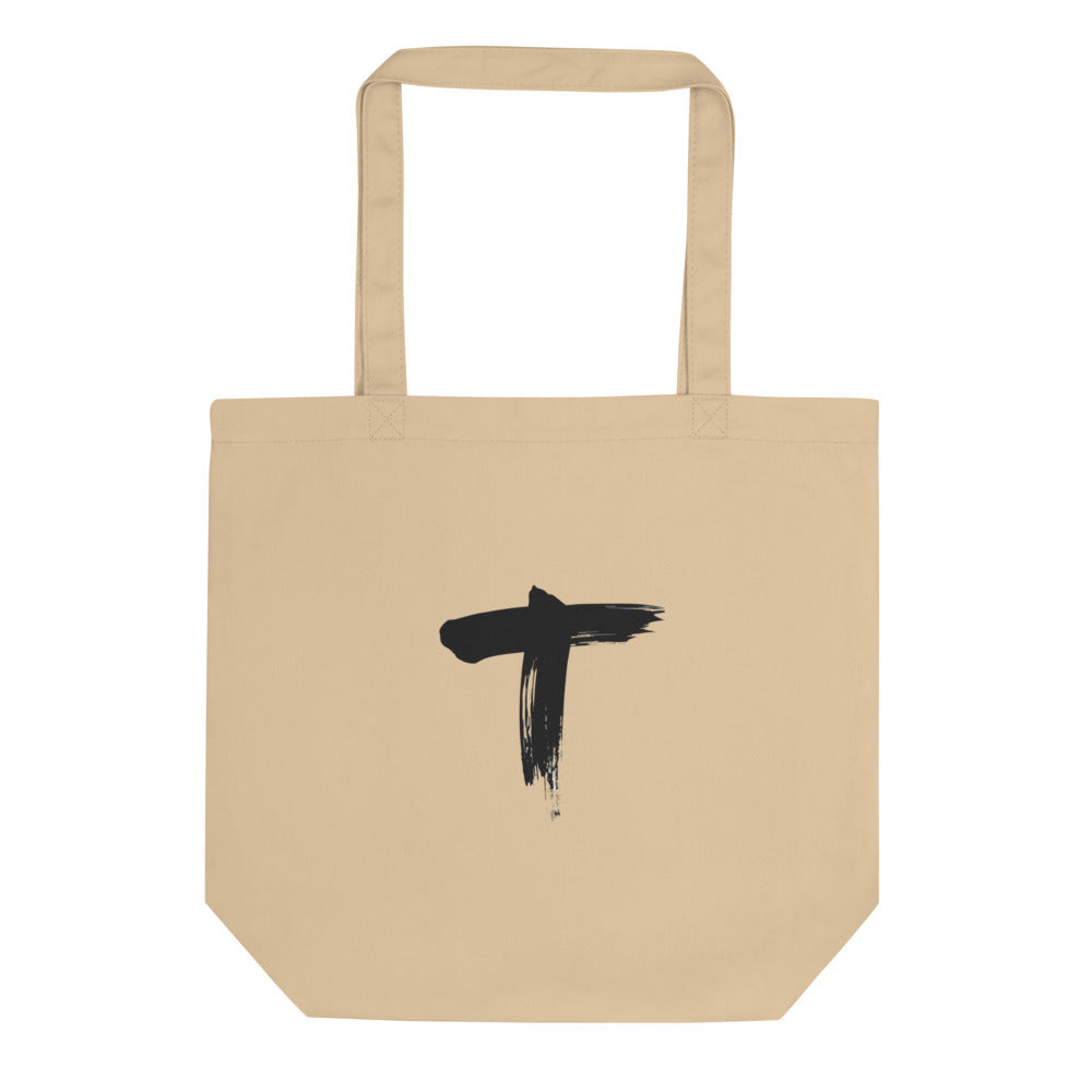 Minimalist black ink sumi-e letter T design printed on a canvas tote bag. Shown on the Bone (Oyster) colorway.