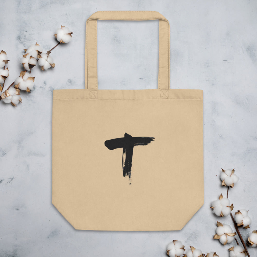 Minimalist black ink sumi-e letter T design printed on a canvas tote bag. Flat lay, Bone colourway.