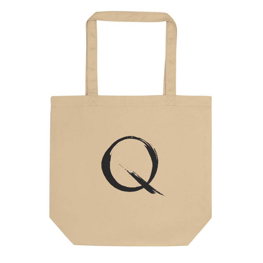 The letter Q rendered in a single minimalist sumi-e brush gesture on a tote bag. Shown on the Bone (Oyster) colorway.