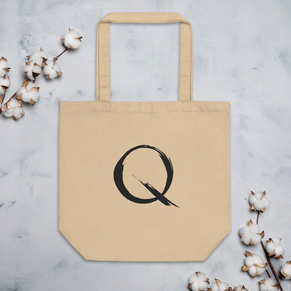 The letter Q rendered in a single minimalist sumi-e brush gesture on a tote bag. Flat lay, Bone colourway.