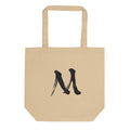The letter M in black sumi-e brush stroke style printed on a minimalist tote bag. Shown on the Bone (Oyster) colorway.
