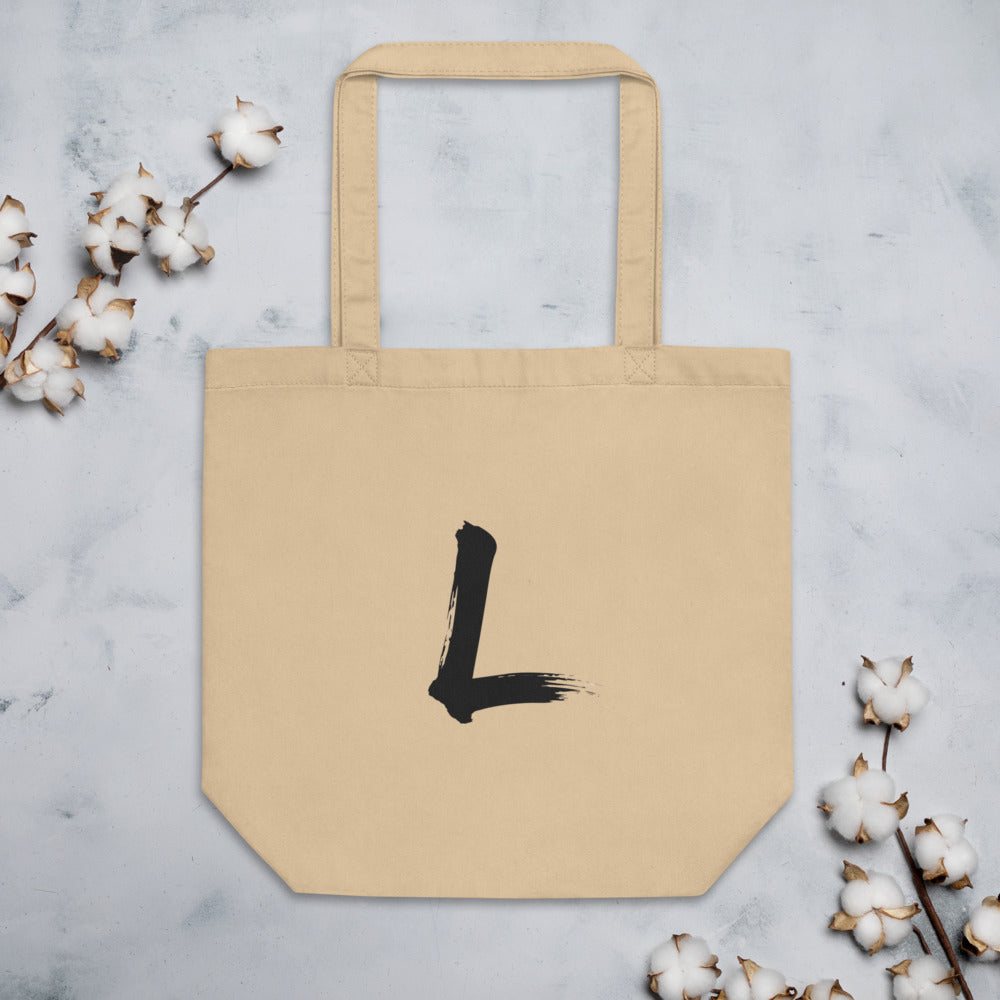 A black sumi-e brushstroke of the letter L printed on a simple tote bag. Flat lay, Bone colourway.