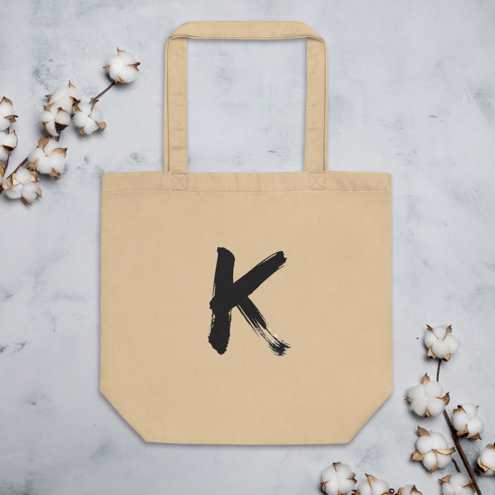 Sumi-e ink brush painting of the capital letter K printed on a canvas tote bag. Flat lay, Bone colourway.