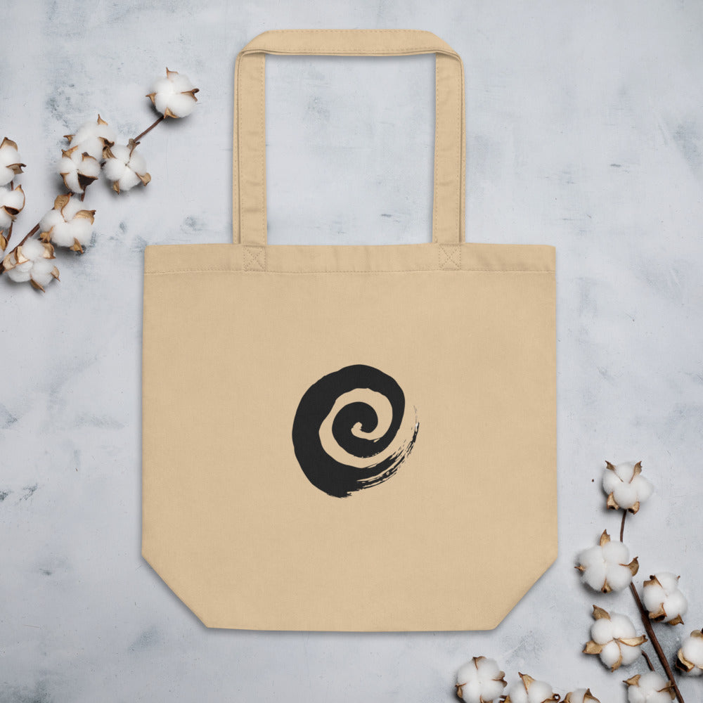 A minimal sumi-e spiral representing a coiled snail shell printed on a tote bag. Flat lay, Bone colourway.