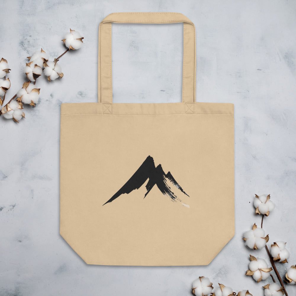 A sharp, minimalist sumi-e ink drawing of a jagged mountain peak printed on a tote bag. Flat lay, Bone colourway.
