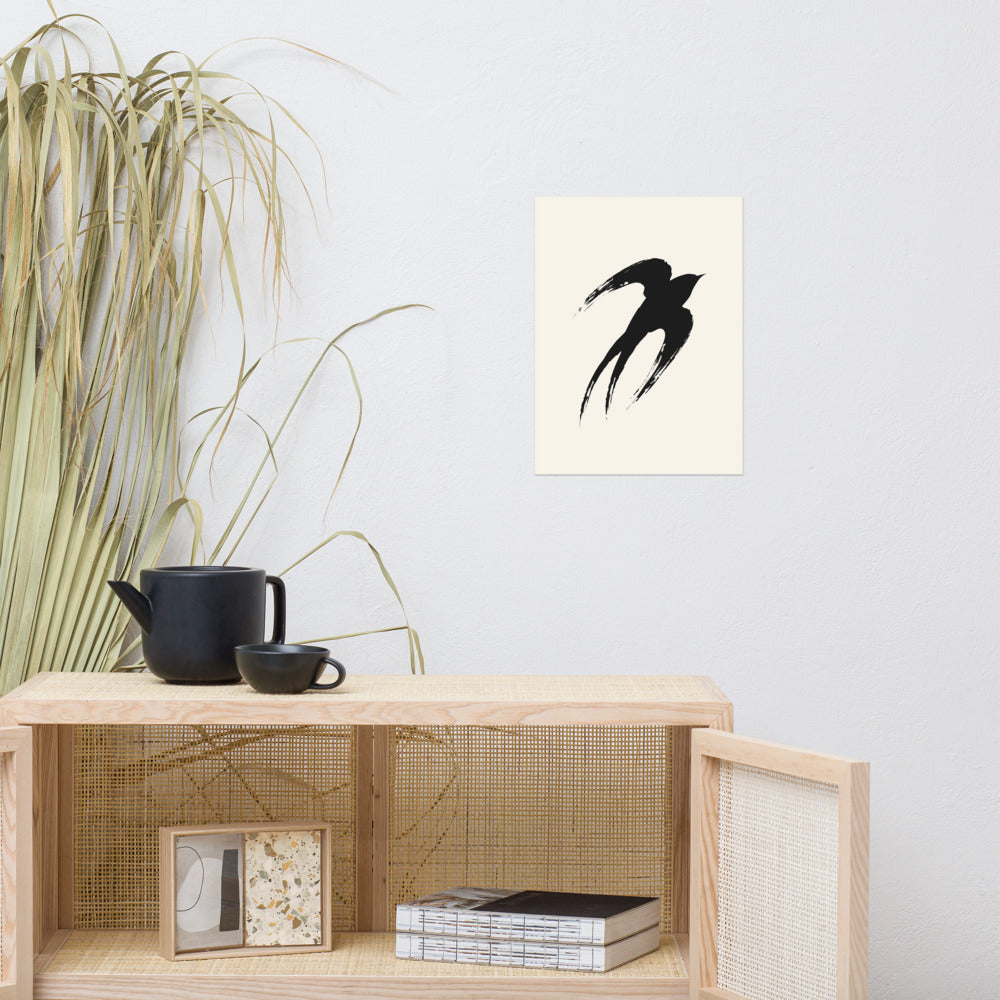 A minimalist sumi-e ink painting of an ascending swallow printed on an art print. Above a rattan cabinet, 12″×16″ size.
