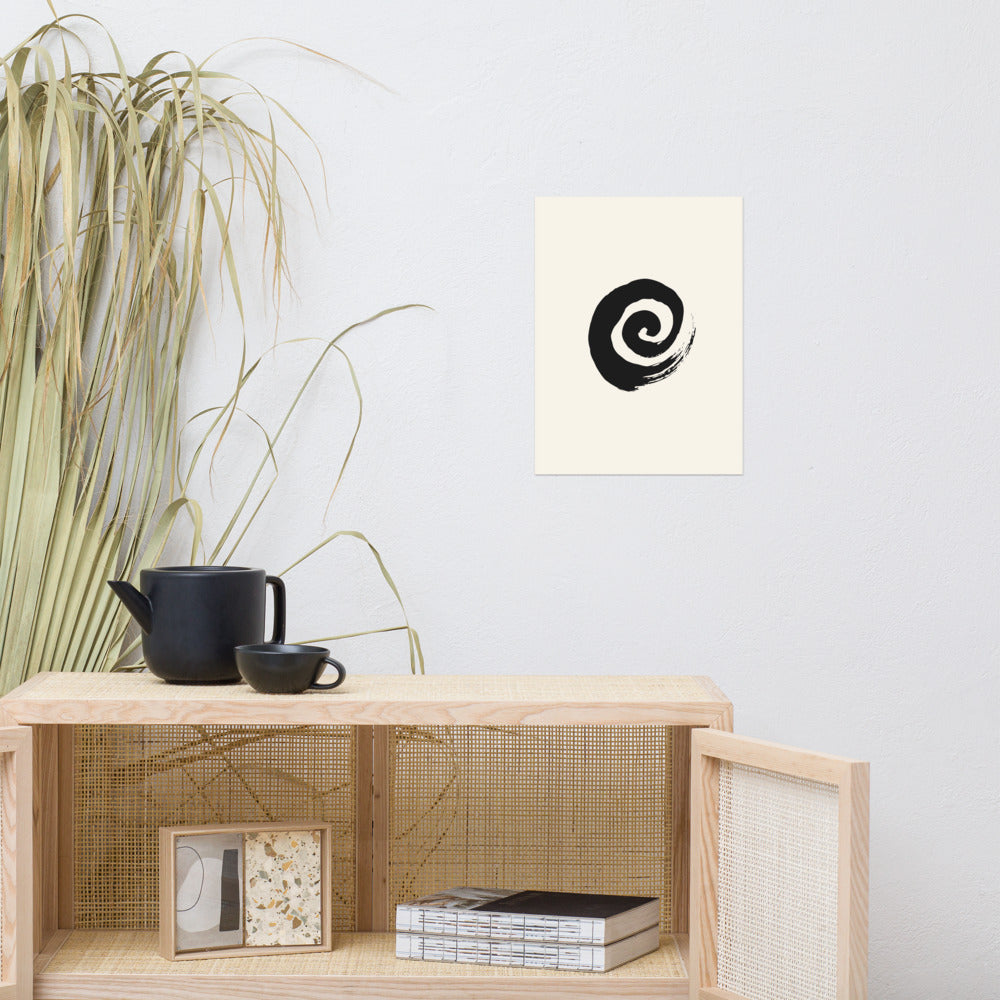 A minimal sumi-e spiral representing a coiled snail shell printed on an art print. Above a rattan cabinet, 12″×16″ size.
