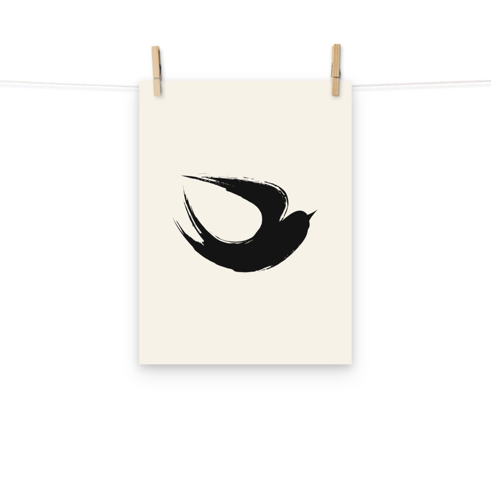 A minimalist sumi-e ink brush painting of a flying swallow on an art print. Hung with wooden pegs, 12″×16″ size.