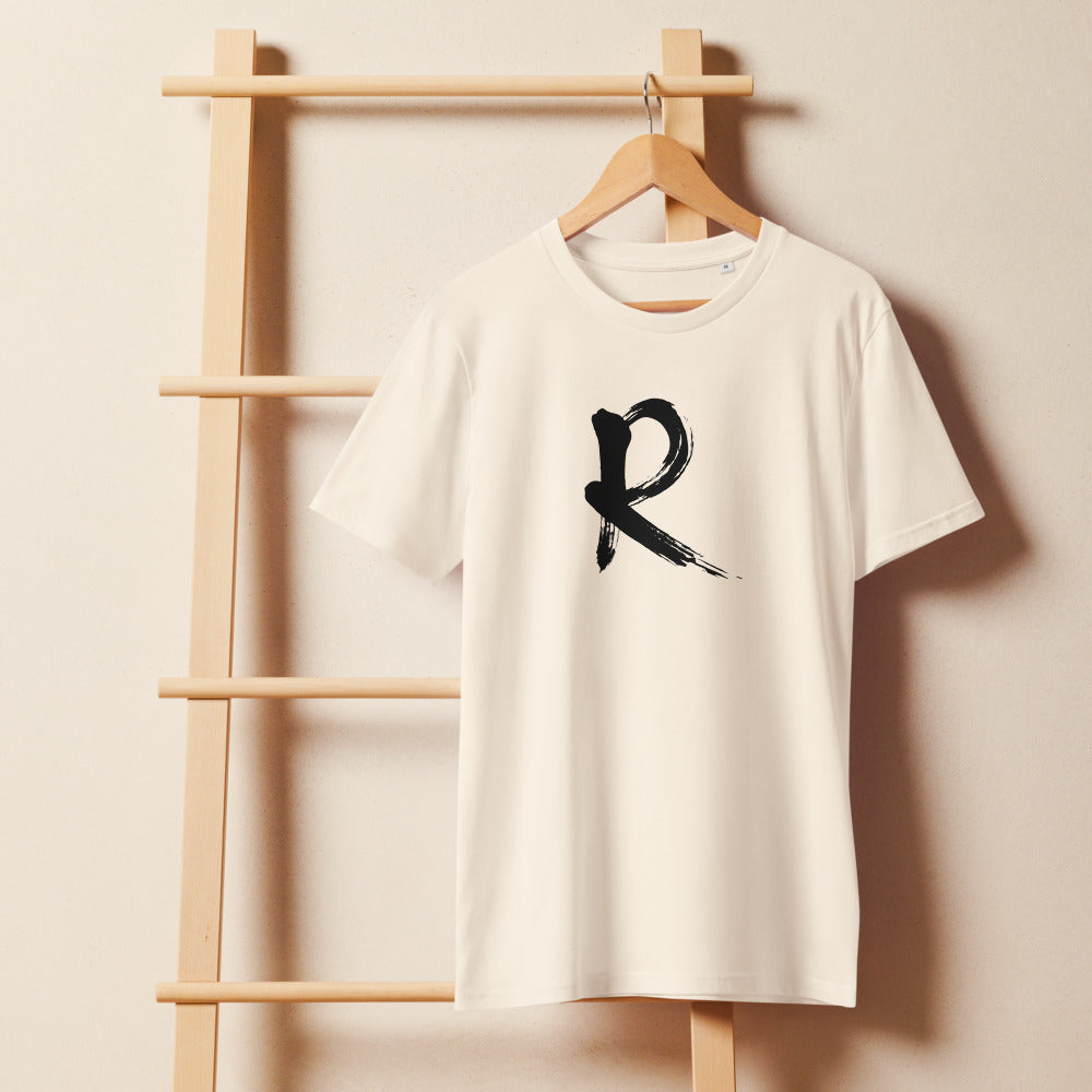 A minimalist sumi-e brush stroke design of the capital letter R printed on a t-shirt. On a wooden hanger, Bone colourway.