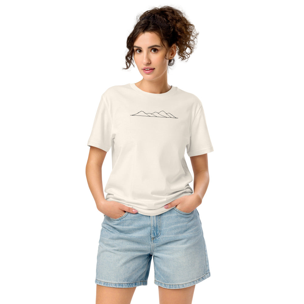A minimalist topographic line art print showing five rolling hill peaks on a cotton t-shirt. Worn by a woman, Bone colourway.